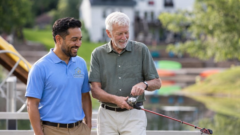 A Cornerstone Caregivers caregiver walking by the water with a senior client holding a fishing rod